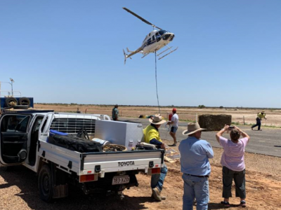 Helicopter dropping fodder in outback with people watching on 